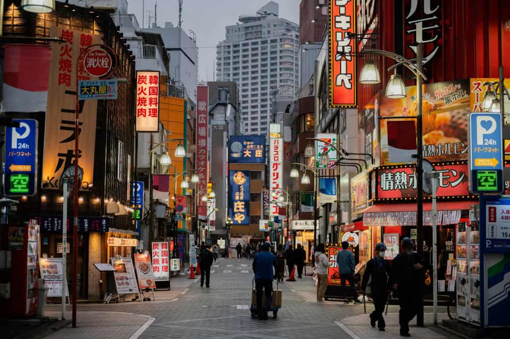 A bustling city street in Japan filled with pedestrians, showcasing a vibrant urban atmosphere and diverse individuals in motion.